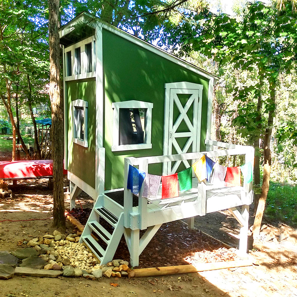 A green, lean-to roof playhouse on stilts in the woods