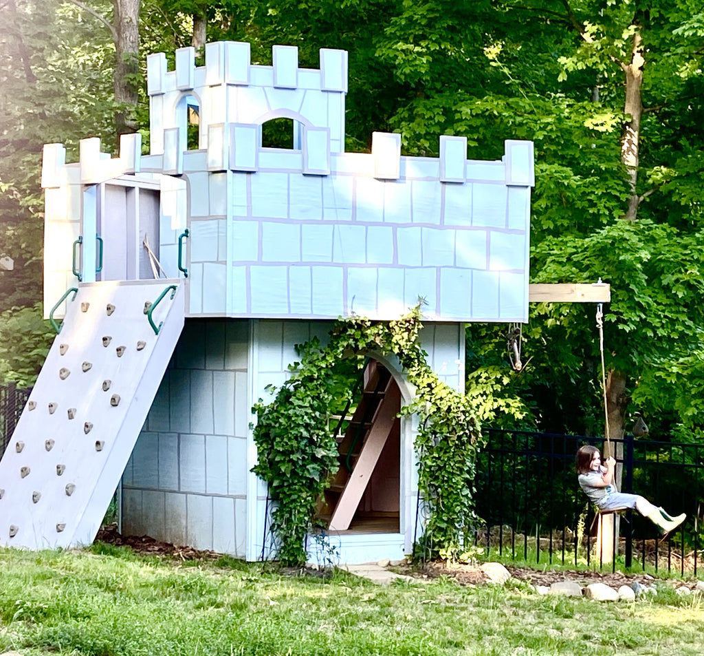 girl swinging on castle playhouse with rock wall