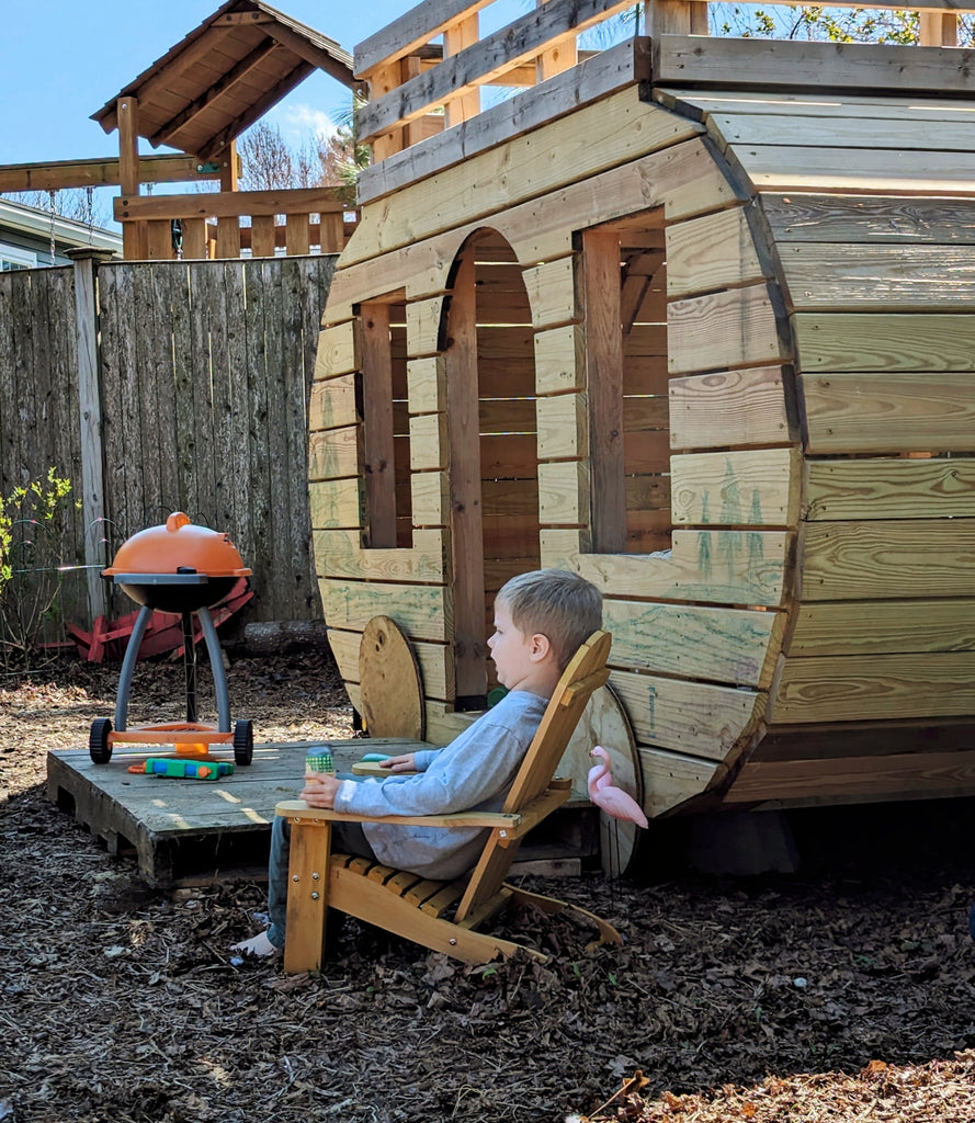 A boy relaxing next to a toy grill and camper playhouse