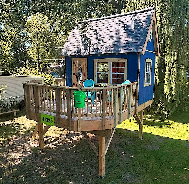 Blue playhouse on posts with wooden deck in a backyard setting