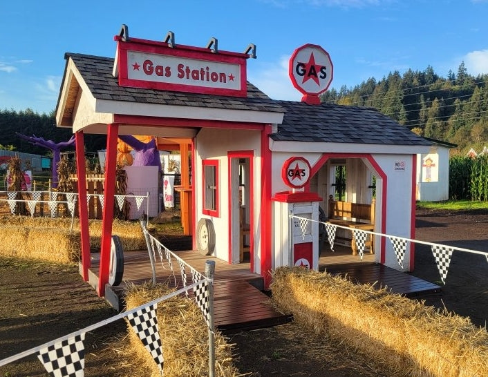Miniature gas station playset with 'Gas' sign and checkered flag with hay bails on raceway.