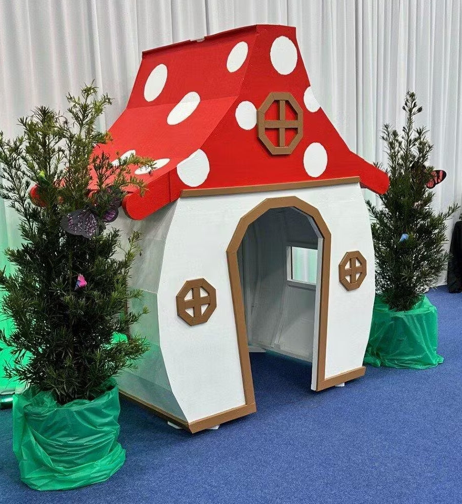 Children's playhouse designed like a mushroom with red cap and white spots, surrounded by green plants on a blue floor.