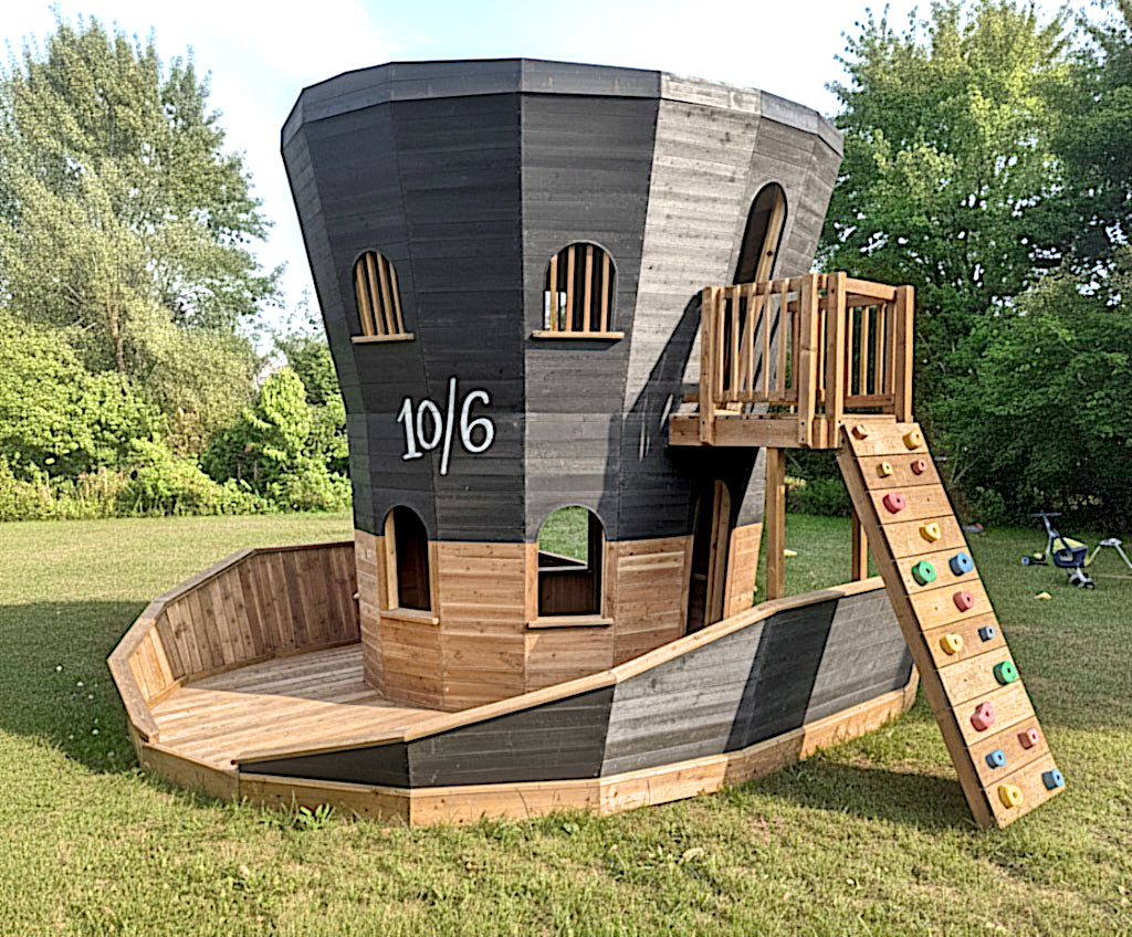 Mad hatter playhouse with upper balcony and rockwall in a backyard setting.