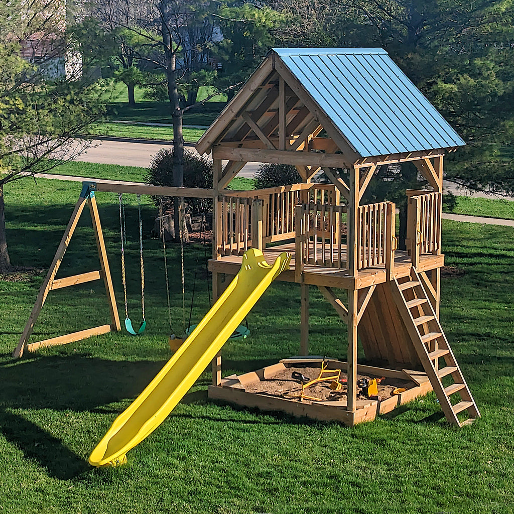 8x8 elevated playset with open gable roof, sandbox, rockwall, slide and swing-set in a sunny front yard with residential street.