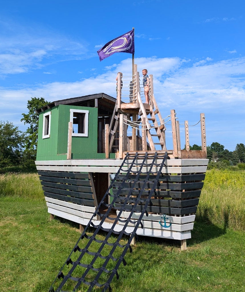 Black and green, large playground pirate ship with boy in crow's nest.
