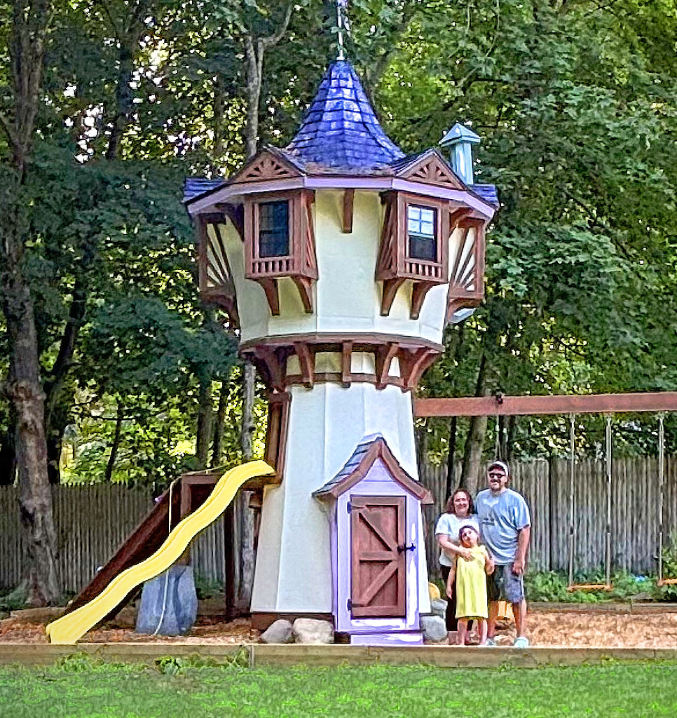 Family next to a Rapunzel's Tower backyard playhouse with slide and storybook decorative aesthetic.