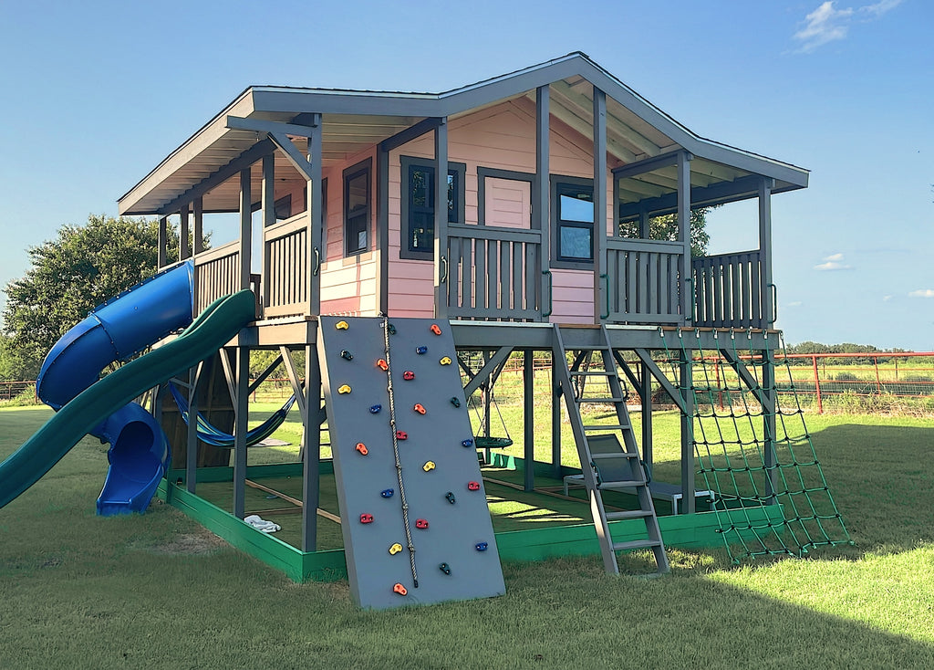 Large gable playhouse on stilts with 360 porch, slides and rock wall.