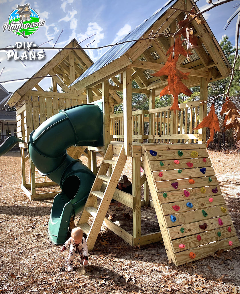Wooden playhouse with green slide and climbing wall, child playing nearby.