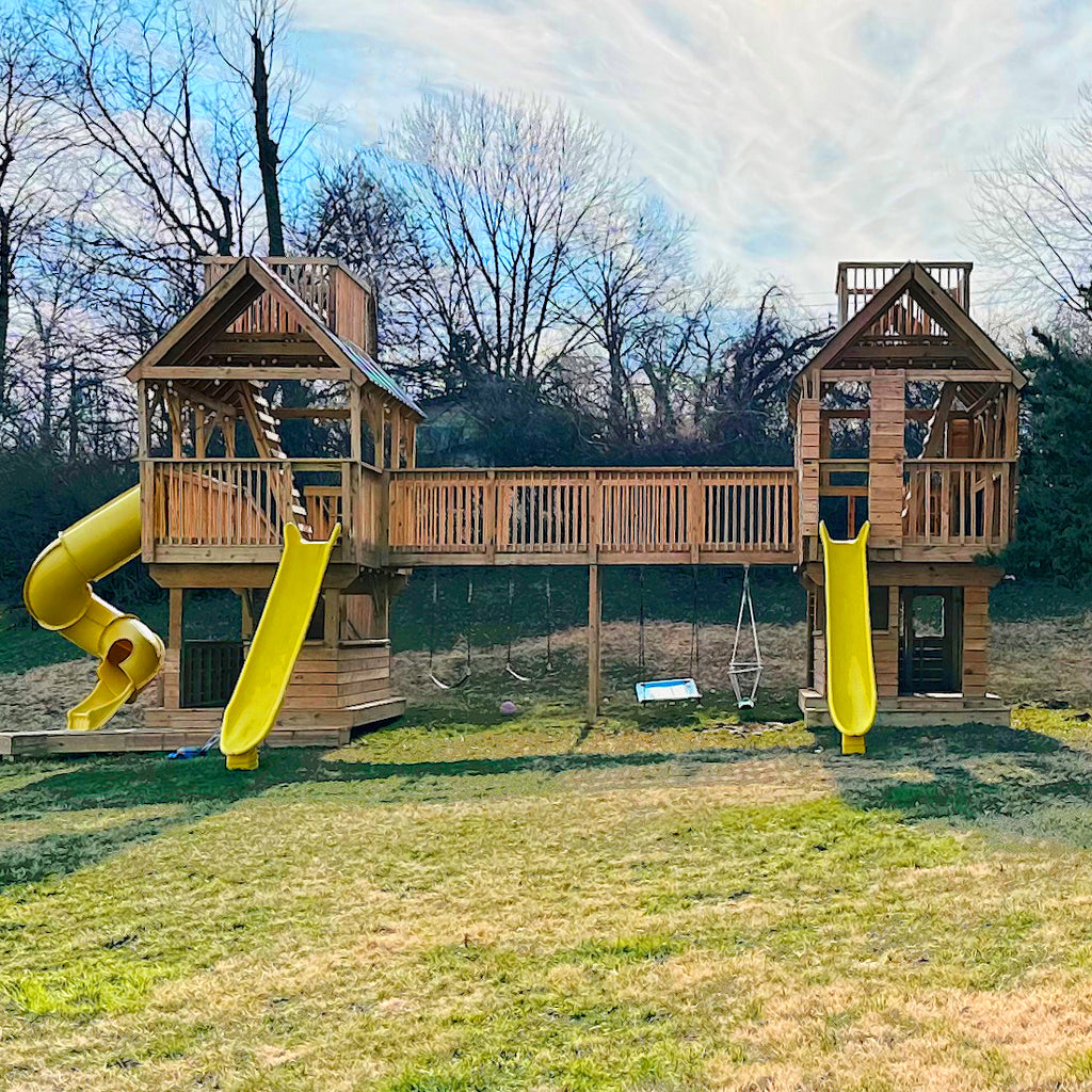 Two large backyard playsets connected by a bridge with roof lookouts