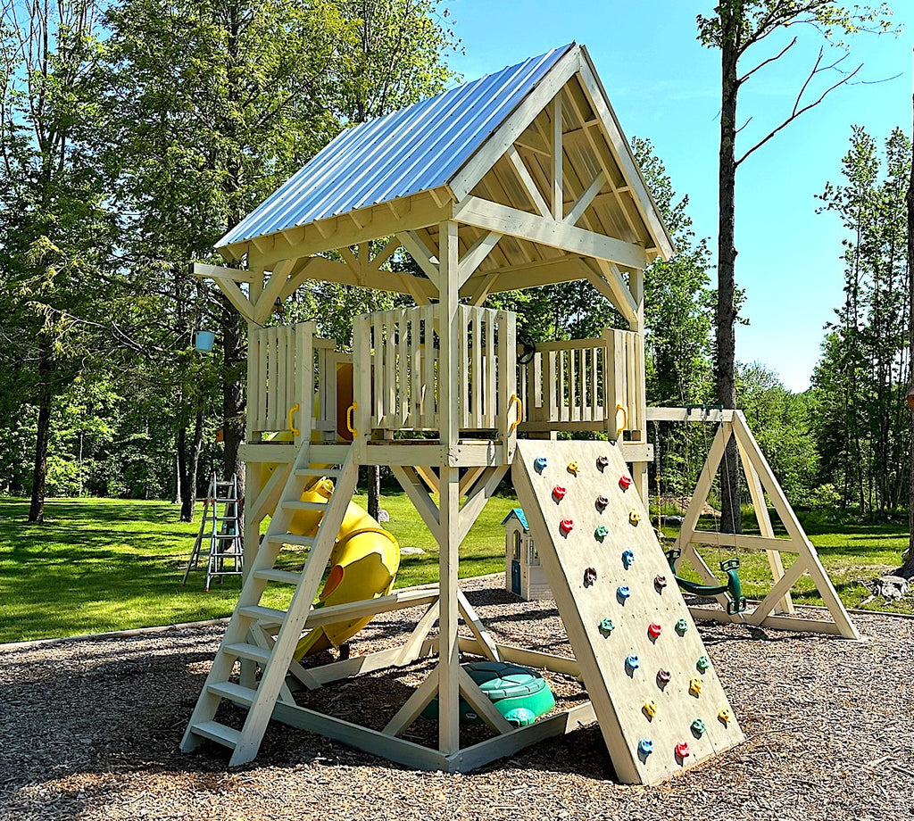 Wooden white backyard playset with gable roof, bucket & pulley, rockwall and swingset.