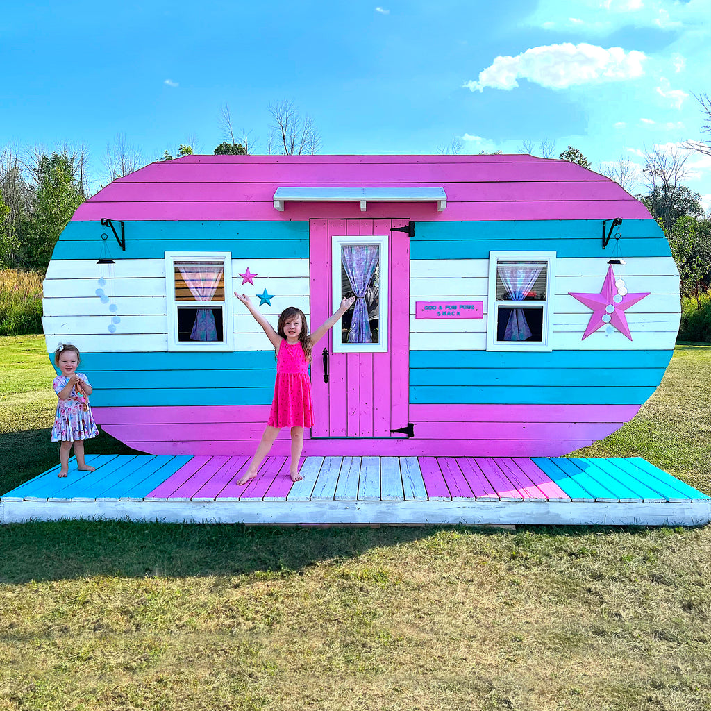 Two girls outside of pink and blue camper playhouse