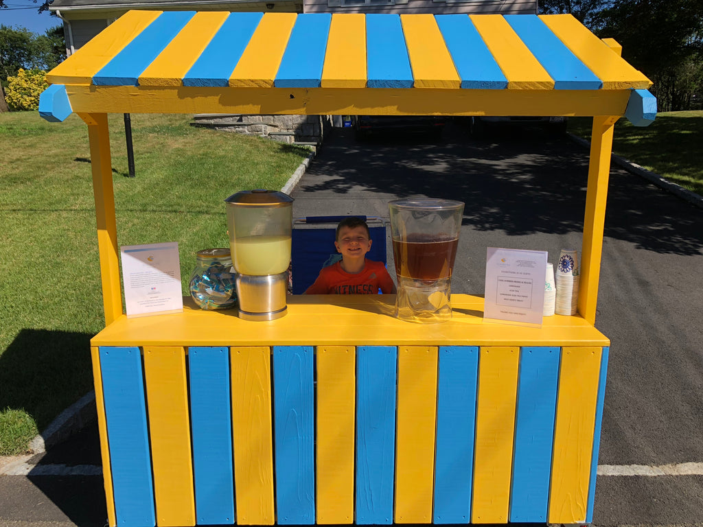 Blue and yellow lemonade stand with a boy and drinks