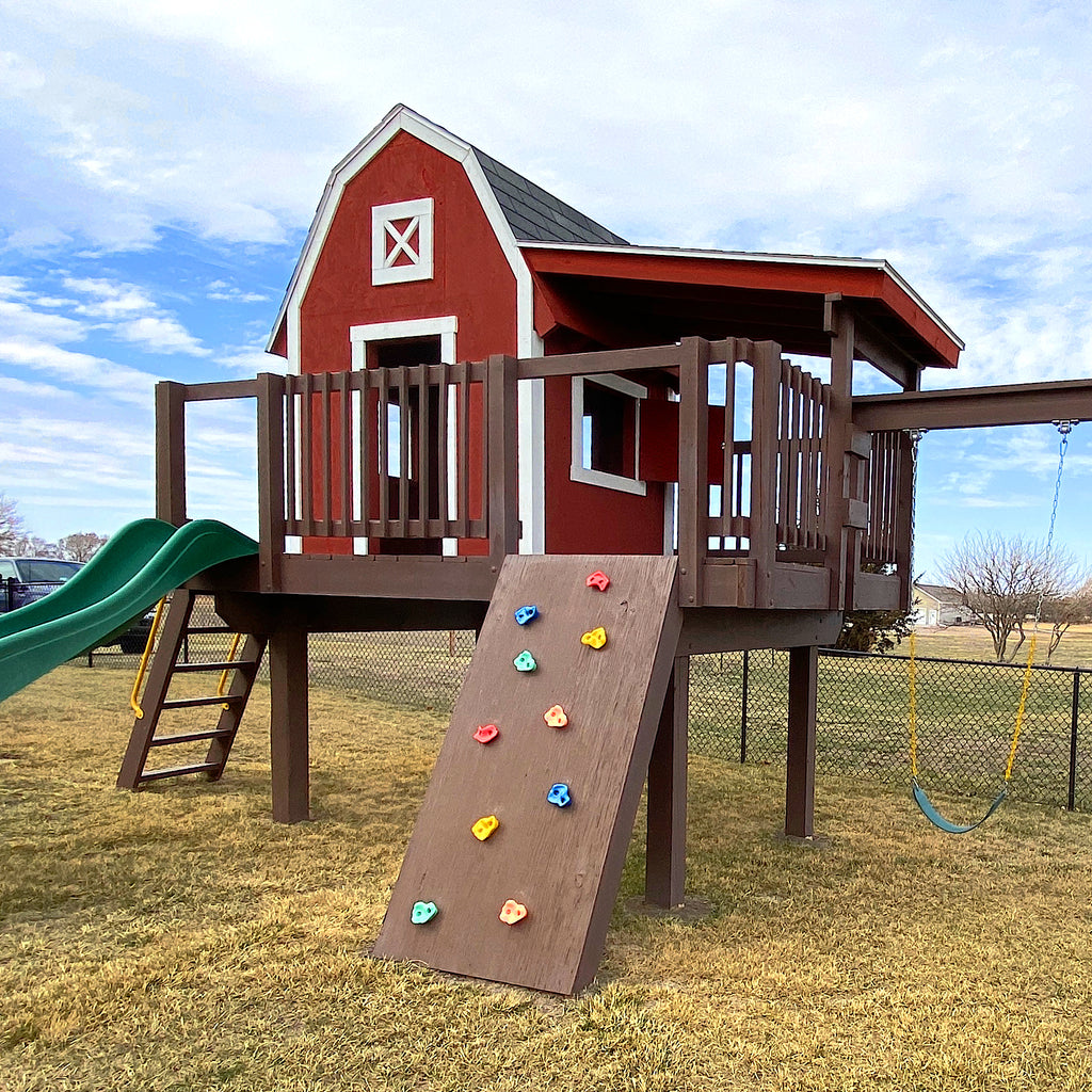 barn playhouse on stilts with slide, rockwall and swings
