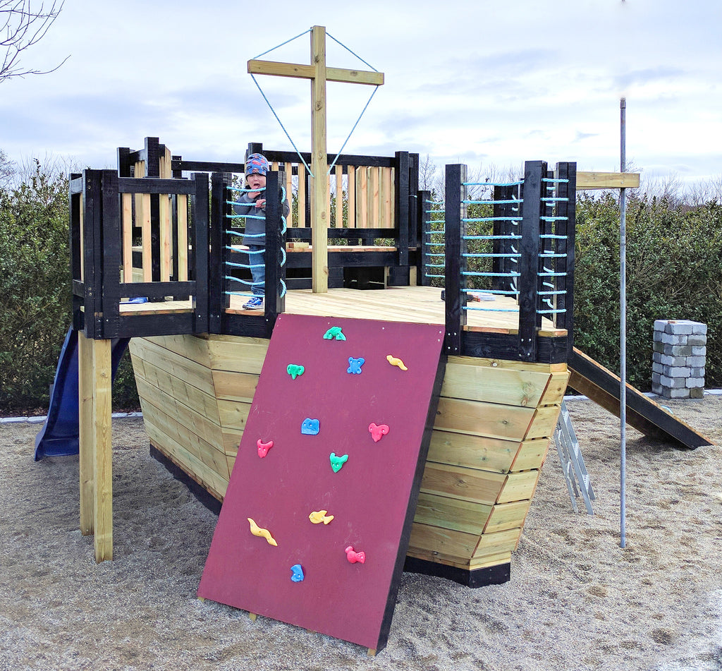 boy playing on a playground pirate ship with slide, gang plank and rock wall.