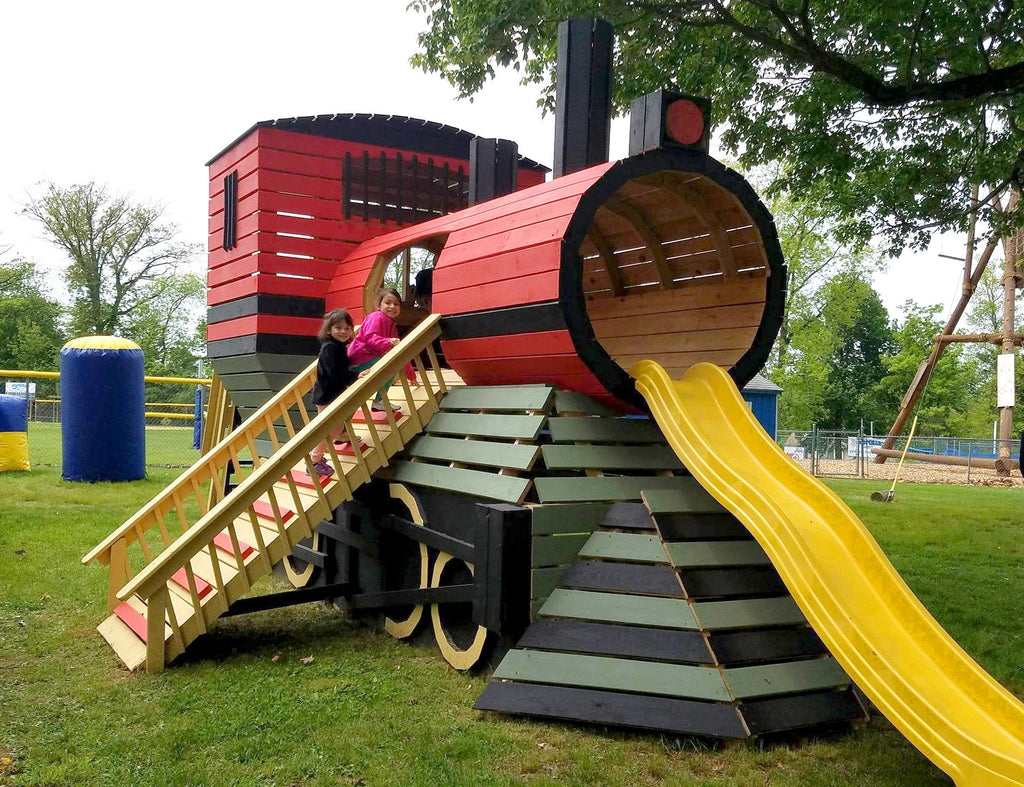 two girls climbing on large wooden train playhouse