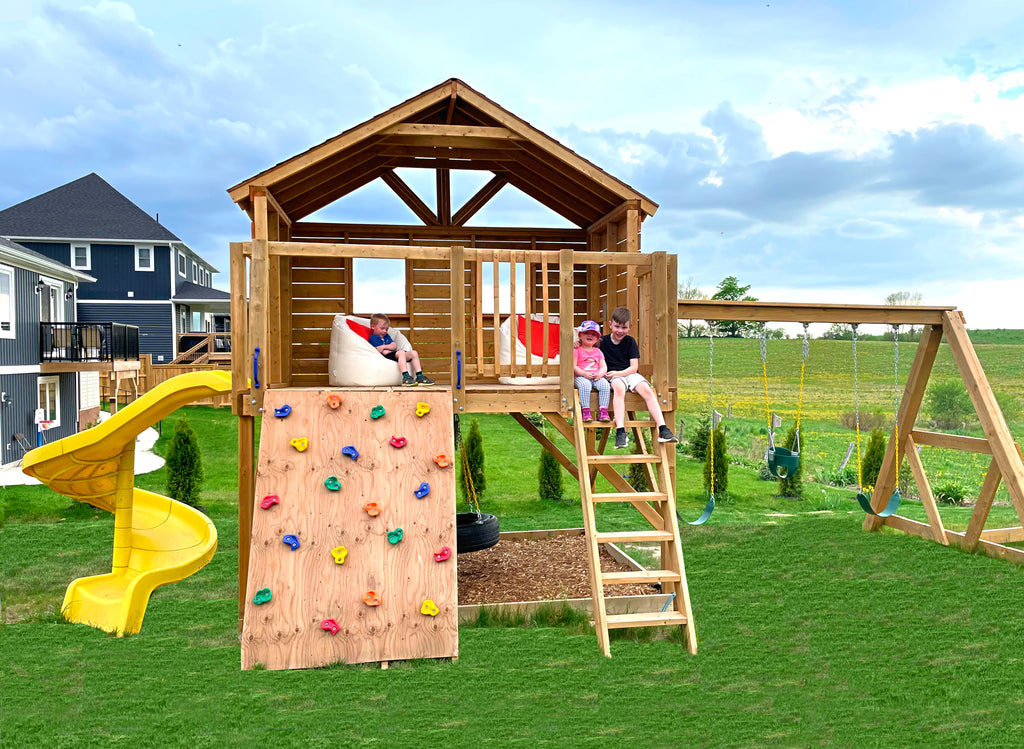3 children enjoying their elevated, open concept playset with slide, rockwall and swingset
